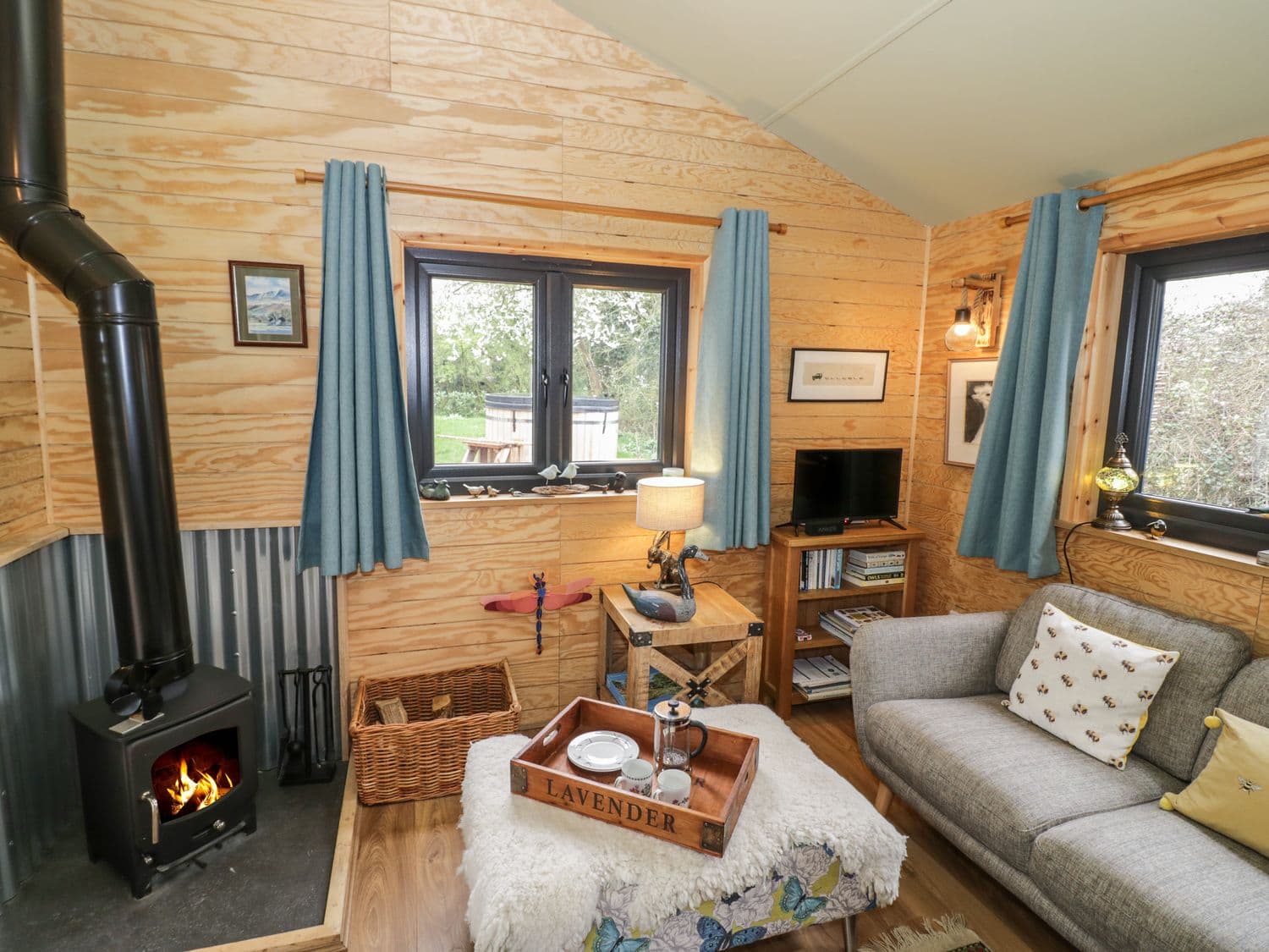 Living room with wood stove, grey sofa and blue cushions at Dragonfly cabin