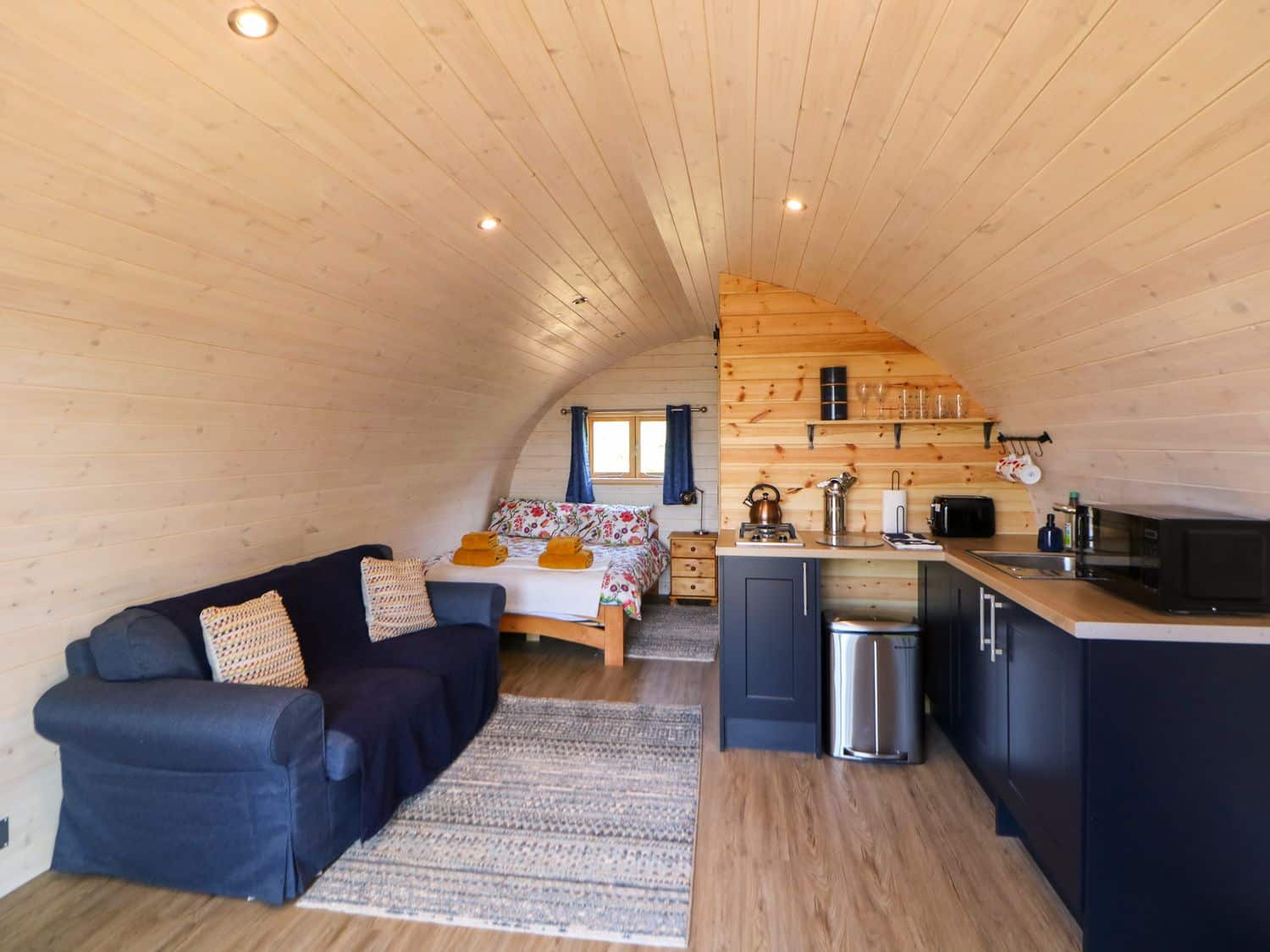Curved timber interior with woodburning stove and cosy seating at Holbein pod