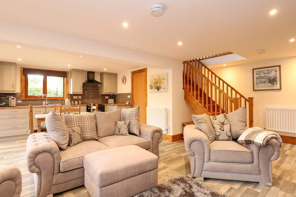 Bright open plan living and kitchen area with beige sofas at Little Lodge